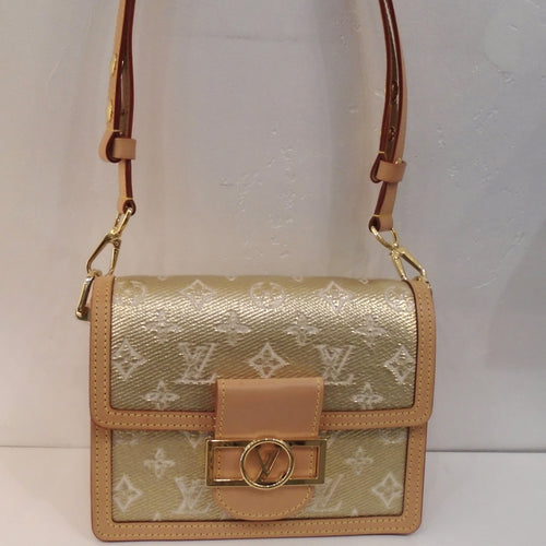 This Louis Vuitton Vintage Monogram Jacquard Mini Dauphine is gold with cream monogram. It has light camel trim and gold hardware. The clasp is a gold rectangle with a circle in its middle and  Louis Vuitton Logo in the center. The interior is camel.