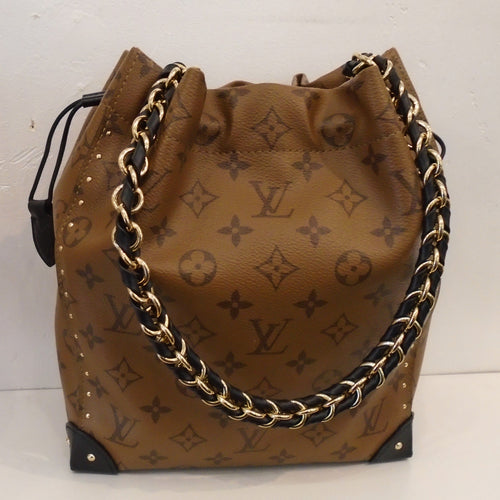 This Louis Vuitton Vintage Monogram Noe' Trunk PM is a bucket bag in a lighter brown with large dark brown monogram pattern. It is reinforced on the bottom corners with black leather. It has a detachable black leather/gold chain strap and the interior of this bag is black.