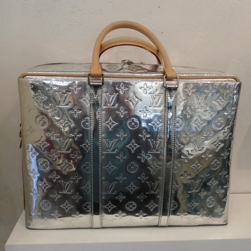 This Louis Vuitton Vintage Mirror Porte Documan Voyage Brief Case is a shiny silver with small Louis Vuitton monogram imprinted in the body of the bag. It has two carrying handles which are camel colored and includes a camel shoulder strap. The interior of the bag is a soft silver.