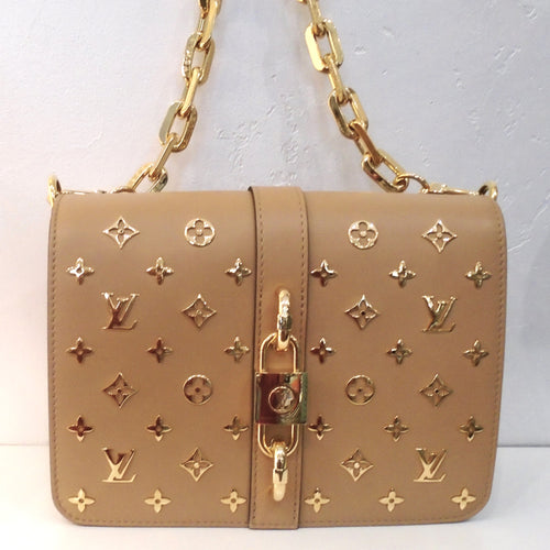 This Louis Vuitton Vintage Metal Rendez/Vous is a tan color with the monogram pattern in gold raised on the bag. It has a heavy gold shoulder chain and a gold lock clasp. The interior of this bag is in the original monogram pattern and colors.