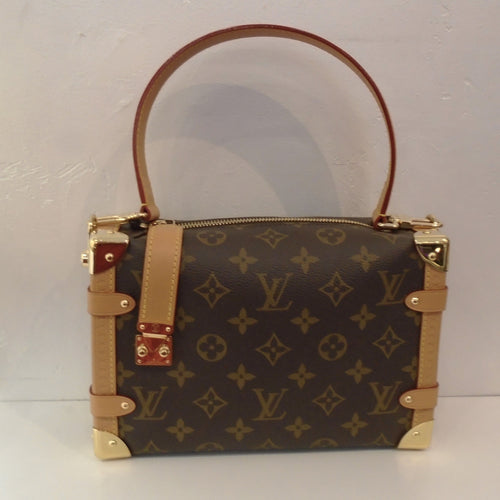 This Louis Vuitton Vintage Monogram Side Trunk MM has camel trim with strips going down the side of the trunk bag and gold hardware corners. It has a hoop carrying handle, zippered top and a camel strap coming down the left front of the bag that latches midway of the bag. The interior of this bag is brown.