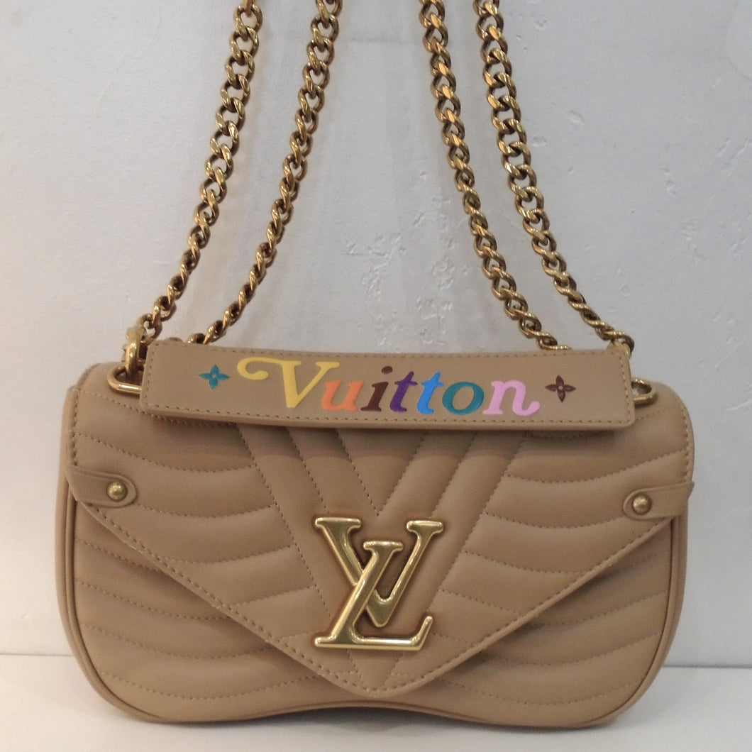 This Louis Vuitton Vintage New Wave PM is a turtle dove color with stitching on the bag that resembles waves. The middle front of the bag has stitching resembling the letter v which is right behind the Louis Vuitton logo. The bag has gold hardware and has a double shoulder chain. It has a detachable handle that has the  word vuitton stitched on it in colorful stitching. The interior of the bag is a light brown.