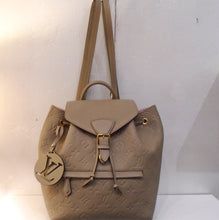 Load image into Gallery viewer, This Louis Vuitton Vintage Turtledove Empreinte Leather Backpack has gold hardware and a drawstring top. It has a flap that comes over the drawstring that has a buckle snap. The backpack has a zippered pocket in the front and a wooden disk with the Louis Vuittion logo cut out of it that hangs by a leather strip. The back straps are adjustable.
