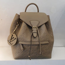 Load image into Gallery viewer, This Louis Vuitton Vintage Turtle Dove Empreinte Montsouirs NMPM has a lower front zippered pocket and a top buckled flap. It has thin sturdy back straps and a sturdy top loop for hanging. The interior is light pink.
