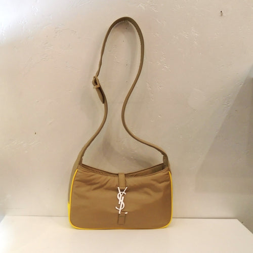 This YSL Light Cork/Yellow Hobo Bag has a long thick adjustable shoulder strap, yellow trim and a white YSL logo on the front of the bag. The top opening of the bag is closed by a strap coming from the back which attaches to the YSL logo that hooks into a loop on the front of the bag. The interior of the bag has the same econyl material.