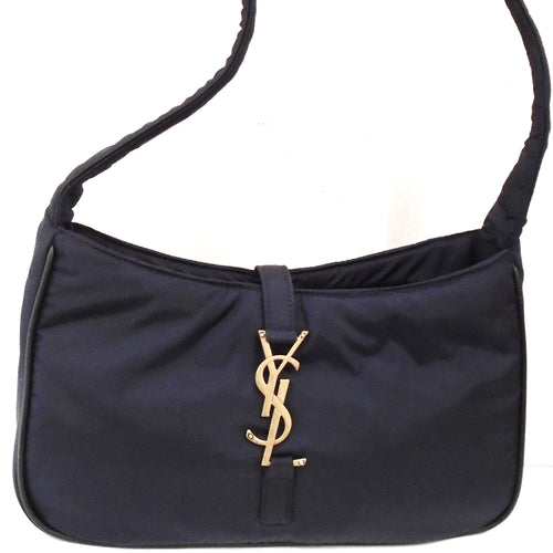 This YSL Navy 5 `A 7 Hobo Bag is a deep navy color and a very soft silky feeling bag. It has gold hardware and the top opening of the bag is closed by hooking the YSL logo, which is connected from the back by a fabric strip into a fabric loop on the front bottom. The interior of the bag is the same econyl material.