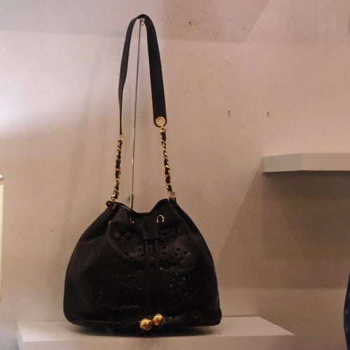 This Chanel Vintage Black Bucket Bag has tiny lacy holes in the shape of interlocking Cs within the body of the bag. It has gold hardware, a drawstring opening and a leather and chain shoulderstrap. A black pouch is included in the bag.