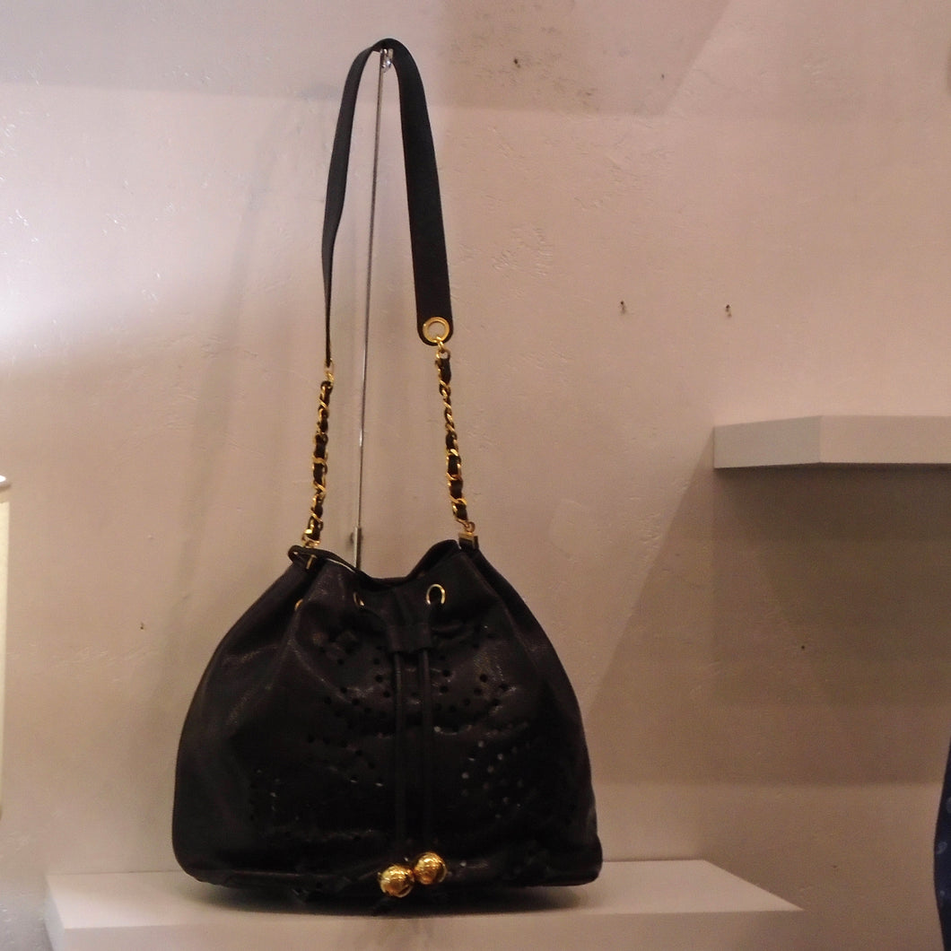 This Chanel Vintage Black Bucket Bag has tiny lacy holes in the shape of interlocking Cs within the body of the bag. It has gold hardware, a drawstring opening and a leather and chain shoulderstrap. A black pouch is included in the bag.