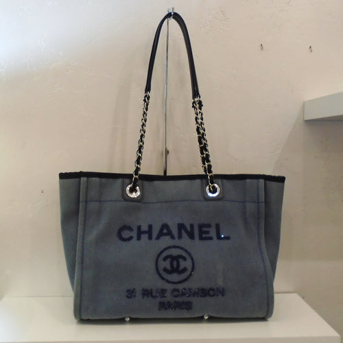 This Chanel Vintage Limited Edition Denim Gst MM Tote has silver hardware with a leather interior. The front has Chanel with the double C Chanel emblem in a circle and a Paris address all stitched in navy blue. The shoulder strap is half leather and half chain link with a strip of leather through the links.