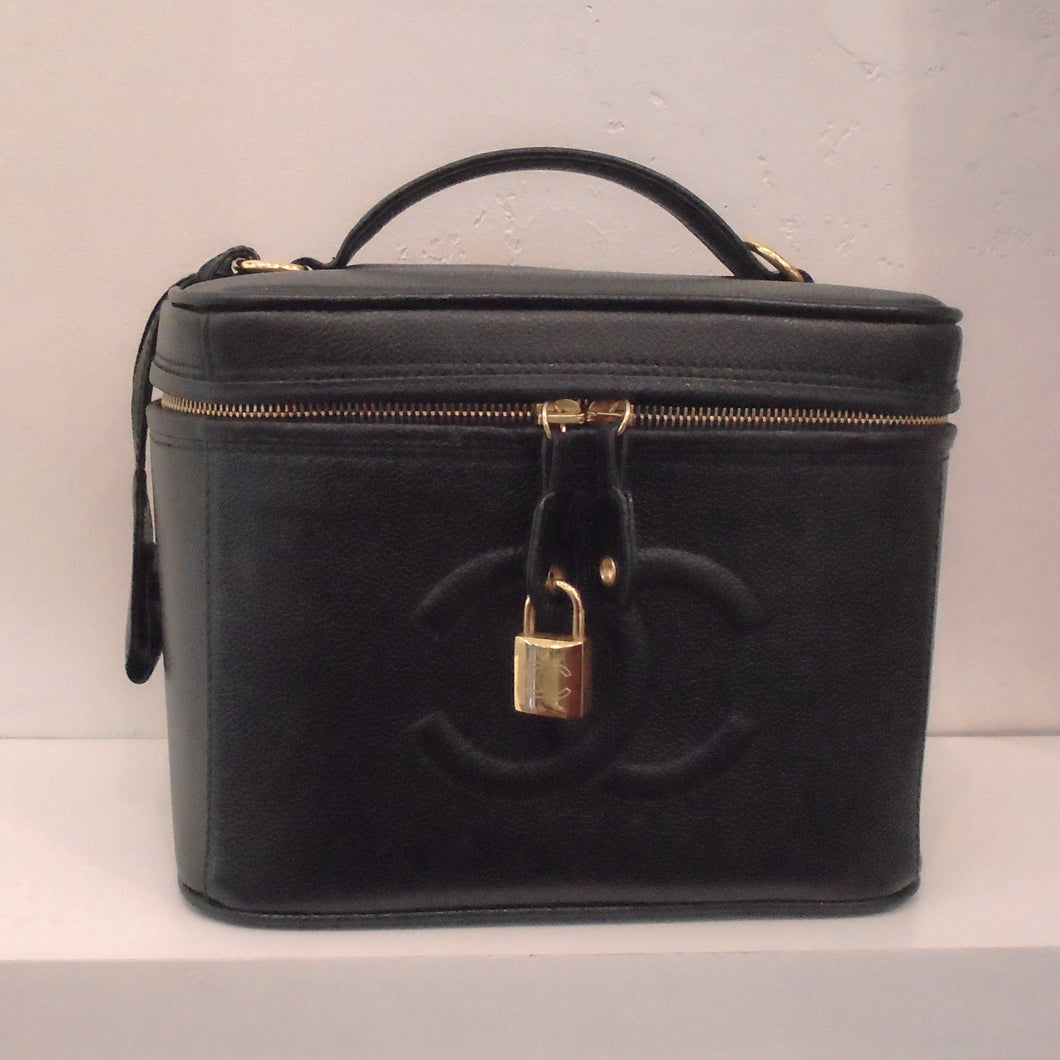 This Chanel Vintage Black Caviar Vanity Bag has the square look of a vanity bag with a zipper running around the top of the bag. It has gold hardware, a lock and key, and a detachable shoulder strap included.