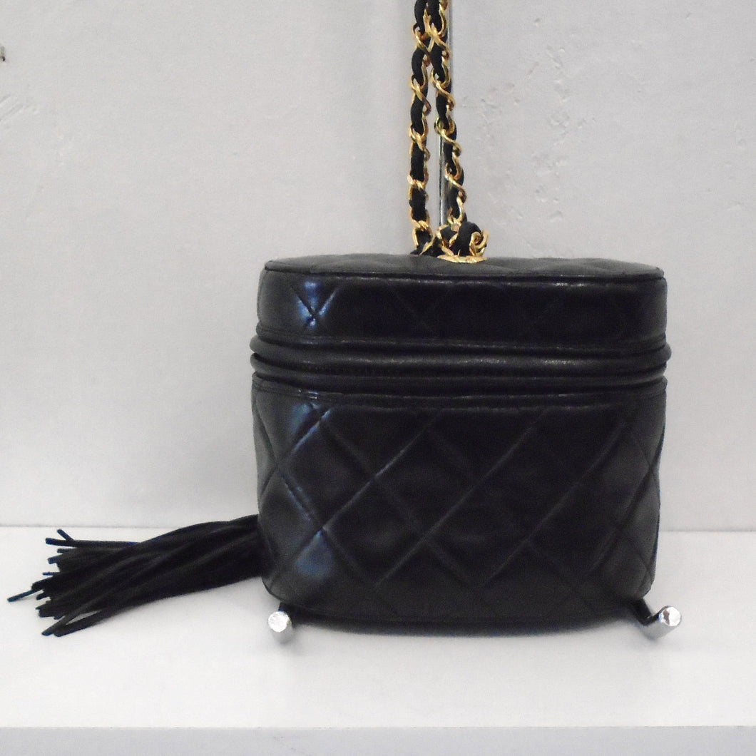 This Chanel Matelasse Labmskin Bag w/Tassel is in Black Lambskin with a zipper that reaches from back around front and back again to give it a top opening. The bag itself is a short barrel style bag. It has a tassel at the end of the zipper, the tassel itself being made of leather strips. It has a gold shoulder chain with a black leather piece interwoven between the chain links.
