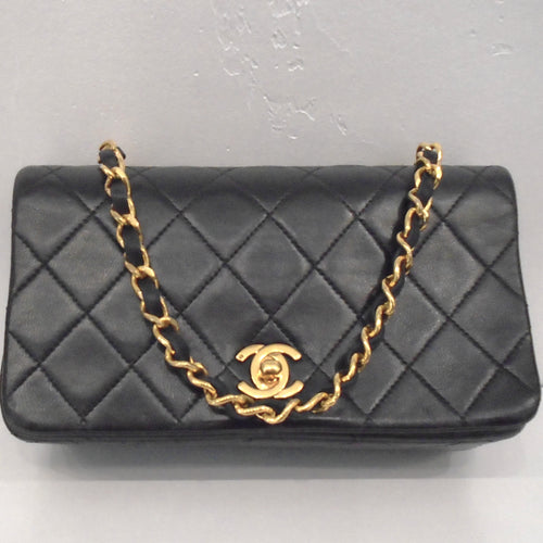 This Chanel Vintage Mini Matelasse Full Flap bag is black in the stitched diamond pattern. The chain is gold with a strip of black leather woven through it. The clasp is gold with the interlocking C's.
