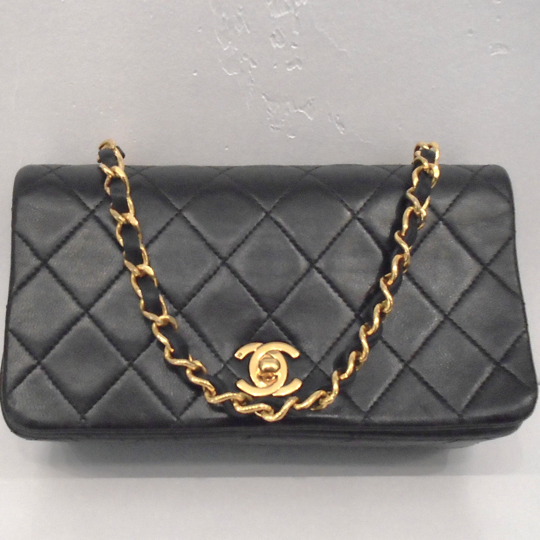 This Chanel Vintage Mini Matelasse Full Flap bag is black in the stitched diamond pattern. The chain is gold with a strip of black leather woven through it. The clasp is gold with the interlocking C's.