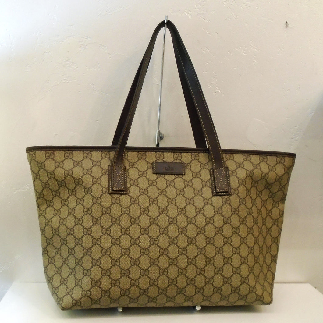 This Gucci Vintage Treated Canvas Joy Tote is light brown with the Gucci logo pattern in a darker brown. The trim is an even darker brown along with the carring handles of the same color. The interior of the bag is a cream color.
