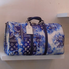 Load image into Gallery viewer, This Louis Vuitton Vintage Keepall #50 Blue Bandana is a very large version of a duffle bag in a tie-dyed blue bandana pattern. The Louis Vuitton monogram pattern is included within this pattern.  It has two navy blue middle straps for support and a shoulder strap is included with the bag.
