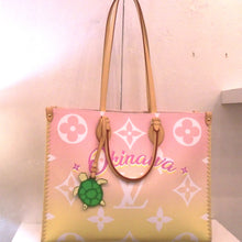 Load image into Gallery viewer, This Louis Vuitton Vintage On The Go GM is a tote with rose pink at the top portion of the bag and yellow on the bottom portion. It has monogram symbols in white and the word Okinawa wirtten across the mid-top portion in pink. The bag has double camel leather handles with a gold and green  turtle attached.
