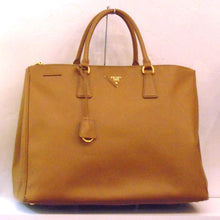 Load image into Gallery viewer, This Prada Caramel Saffiano Leather Large Tote has gold hardware, double carring handles and a key holder attached to the handles. It has a small guitar pick shaped prada name tag on the front and the inside is a silky green.
